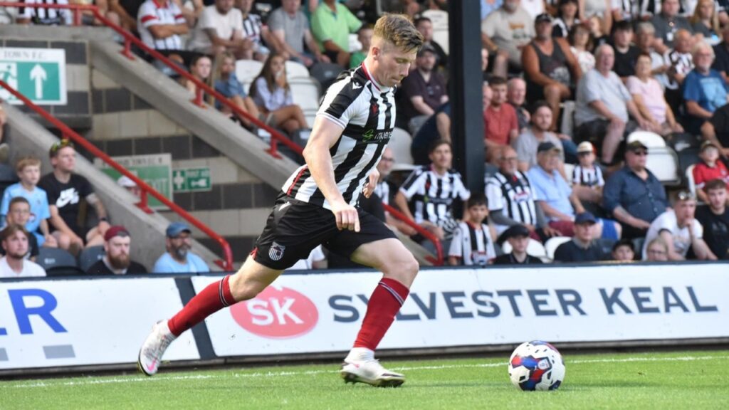 A photograph of Harry Clifton, a GTFC player, kicking a football on the pitch